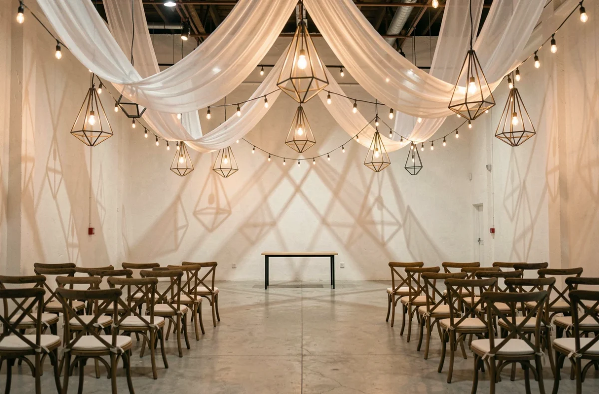 Scénographie lumineuse de mariage avec guirlandes de bulbes Edison et drapés transparents suspendus au plafond en remplacement d'un décor massif